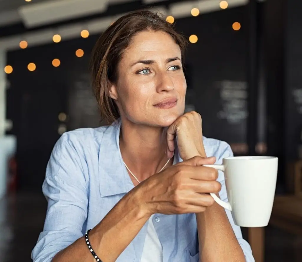 Thoughtful mature woman sitting in cafeteria holding coffee mug while looking away. Middle aged woman drinking tea while thinking. Relaxing and thinking while drinking coffee.