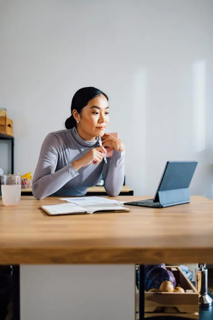 Beautiful Asian businesswoman reading something on a digital tablet at kitchen desk.