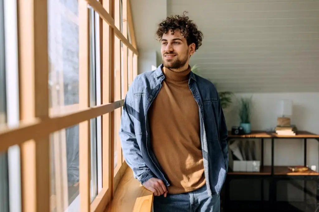 Portrait of young handsome man looking through the window at the apartment