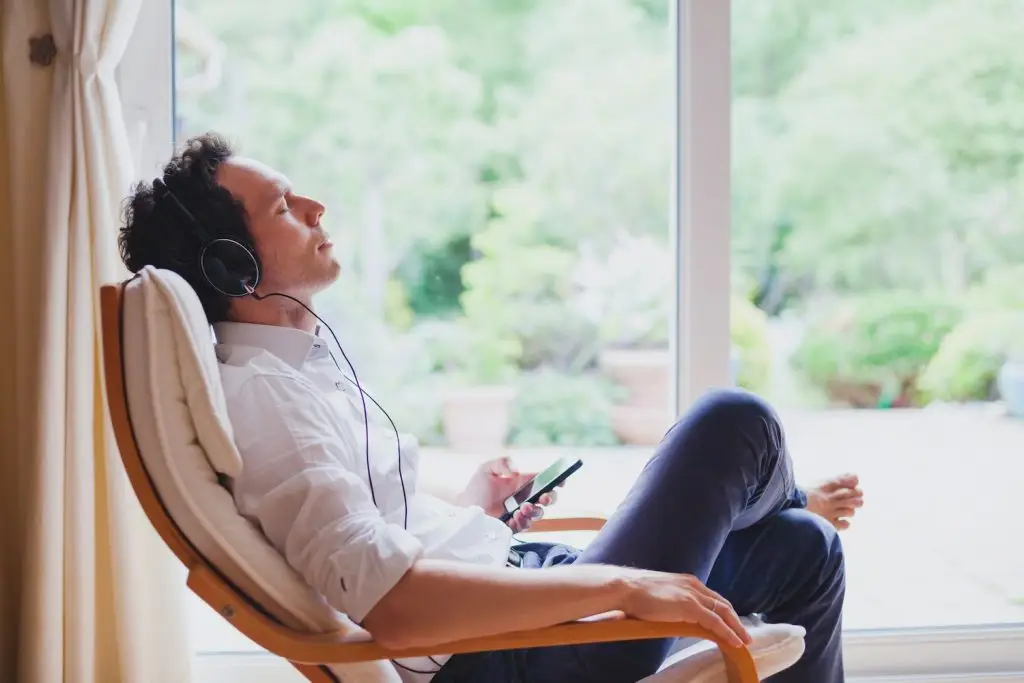 listening relaxing music at home, relaxed man in headphones sitting in deck chair in modern bright interior
