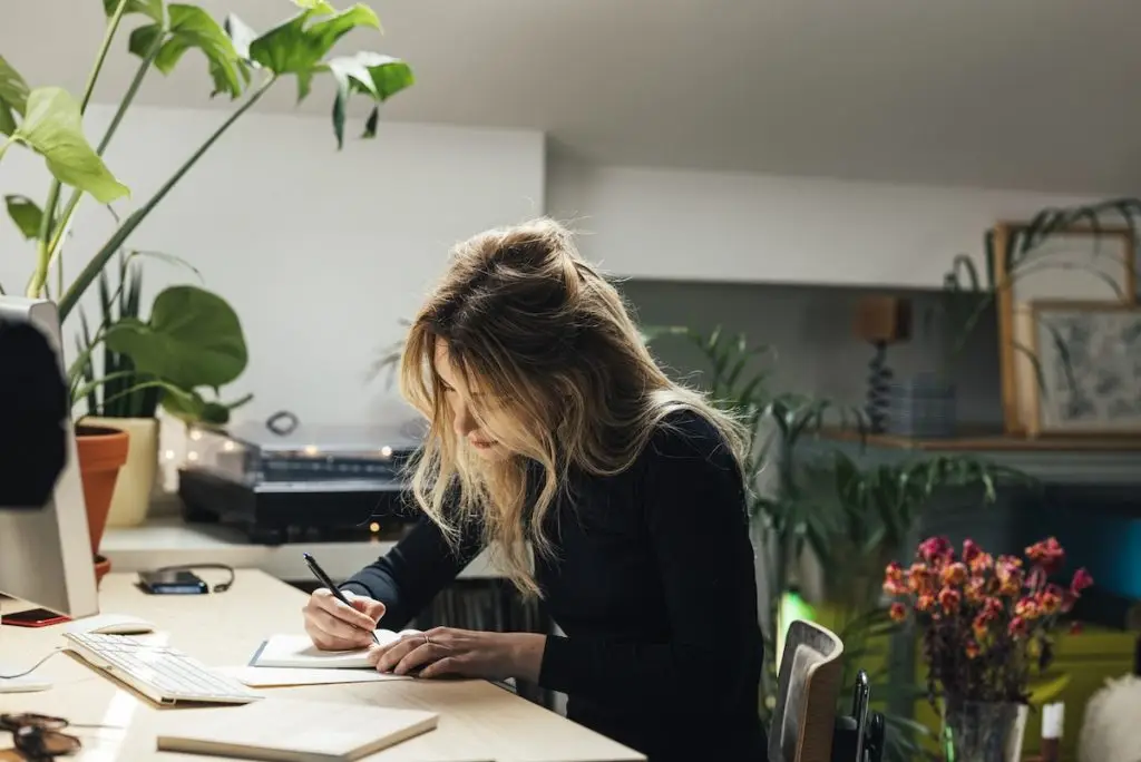 Beautiful blond woman making a to do list while sitting behind a desk in her living roomv