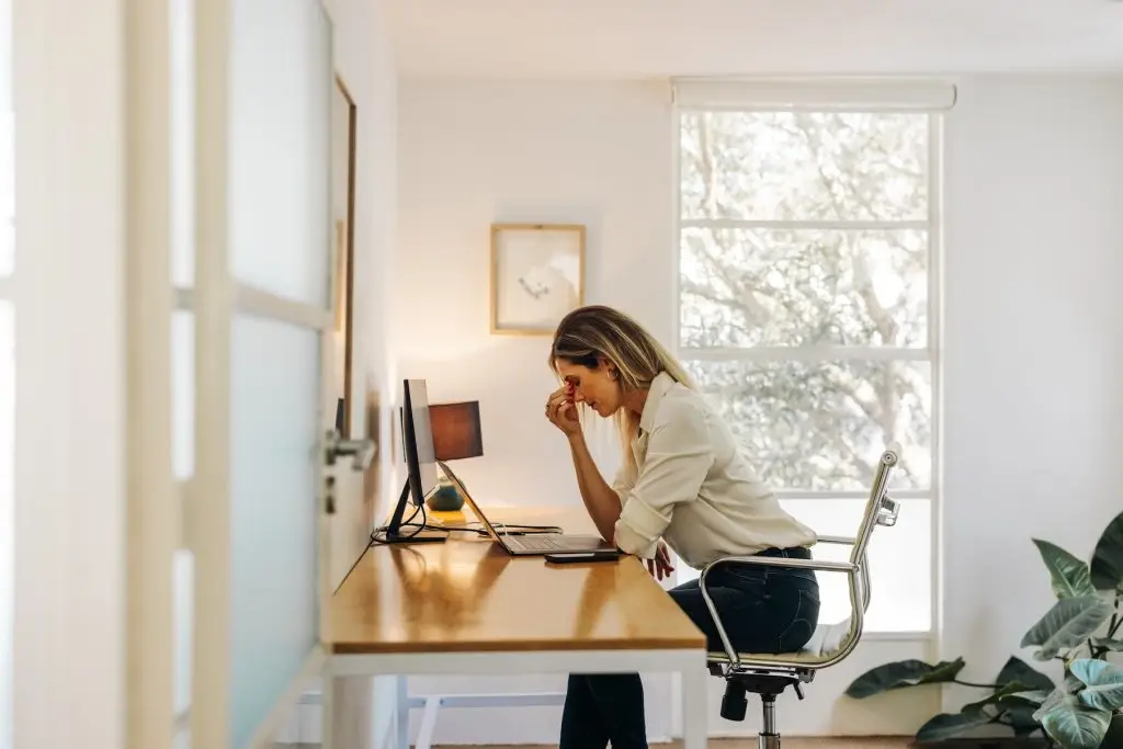 Exhausted businesswoman having a headache in her office. Overworked businesswoman experiencing work fatigue while siting in front of a laptop.