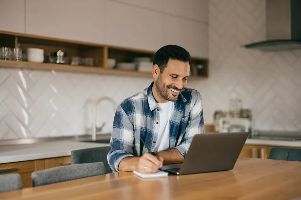 Smiling man working online, writing some notes, making plans.