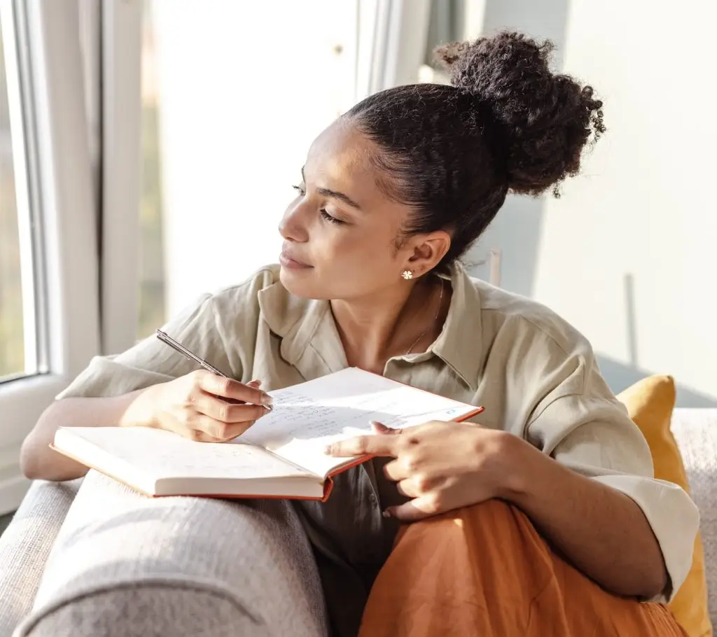 A young woman is at home, she is sitting on the sofa in the living room and writing notes