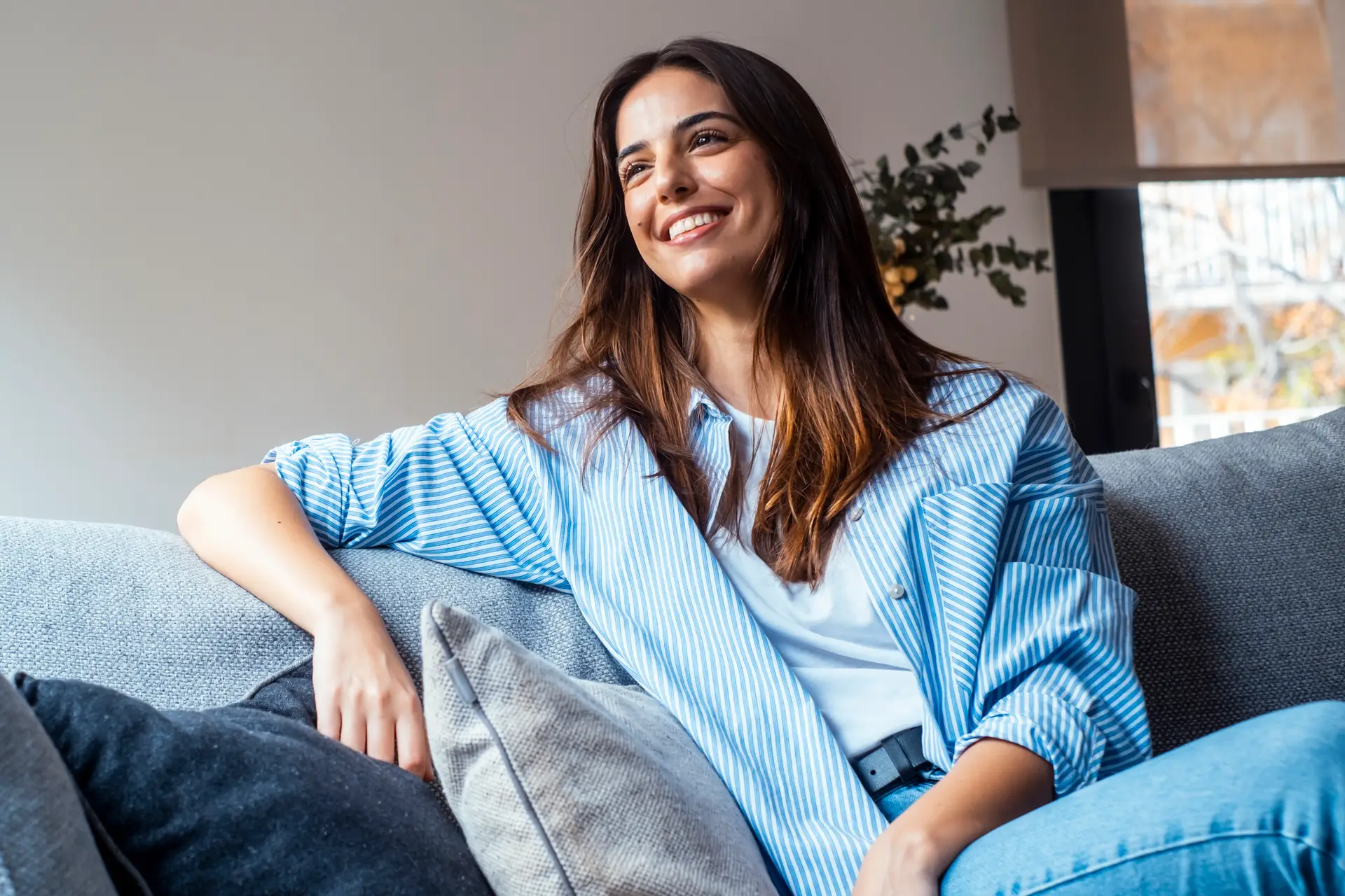 Relax and unwind. Young beautiful brunette woman with blissful facial expression smiles alone on the sofa. Portrait of relaxed woman resting at home.